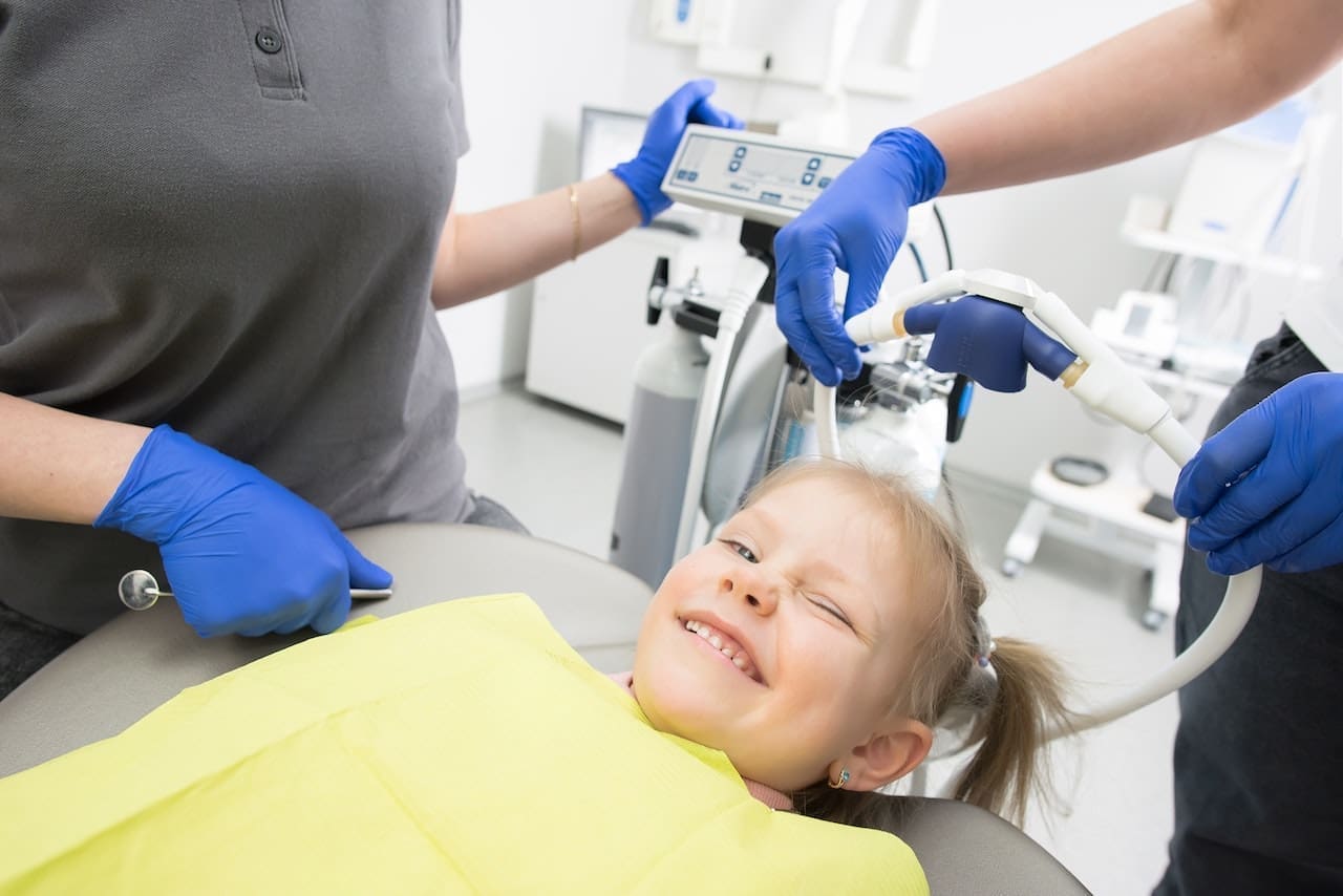 A child sitting in a dental chair, receiving a teeth cleaning from a dentist