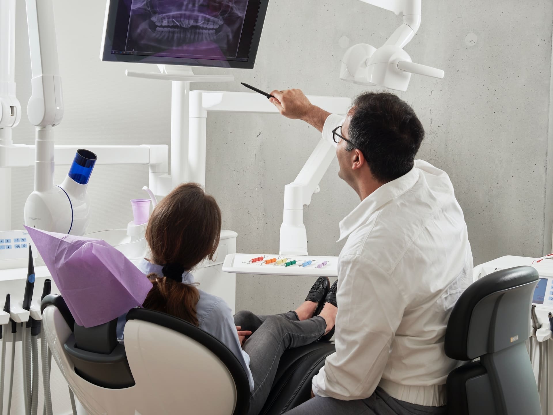 A dentist pointing at a dental X-ray film, explaining the findings to a patient in a dental office.