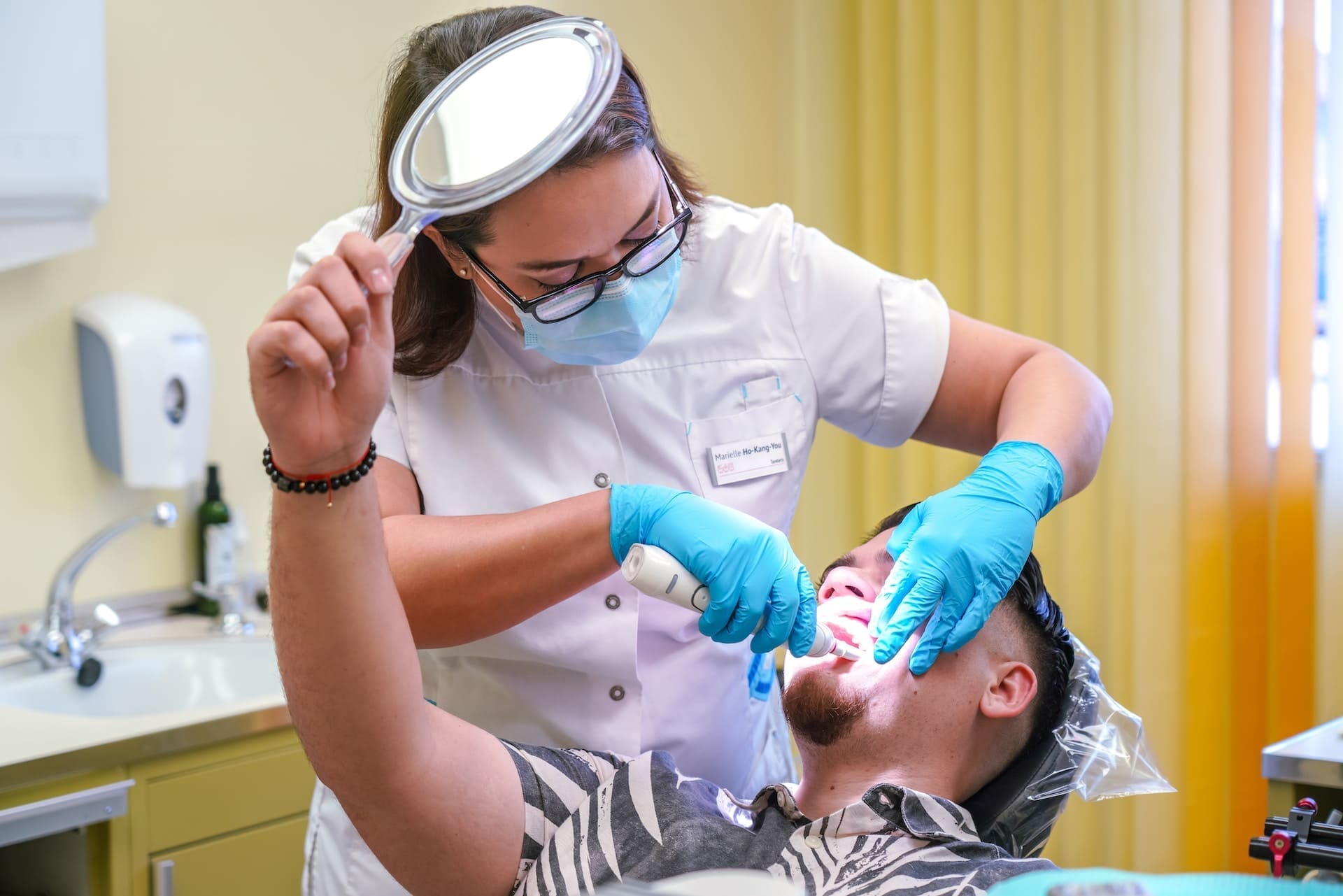 A man undergoing a teeth whitening procedure in a dental chair, with a dentist applying treatment.